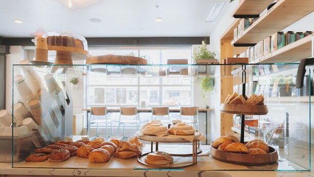 A bakery display with various pastries and bread, a coffee machine, and a seating area with tables and chairs. - The Wren (Missoula)