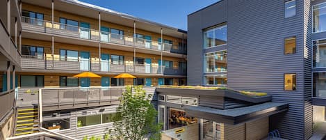 Un edificio moderno de varios pisos con balcones, mobiliario exterior y un jardín en la azotea.