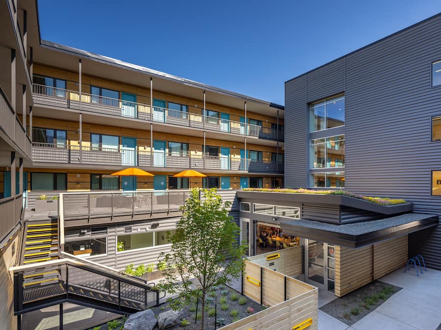 A modern multi-story building with balconies, outdoor seating, and a rooftop garden.