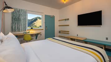 Une chambre d’hôtel équipée d’un lit, d’un bureau, d’une chaise, d’une télévision et d’une fenêtre donnant sur les montagnes.