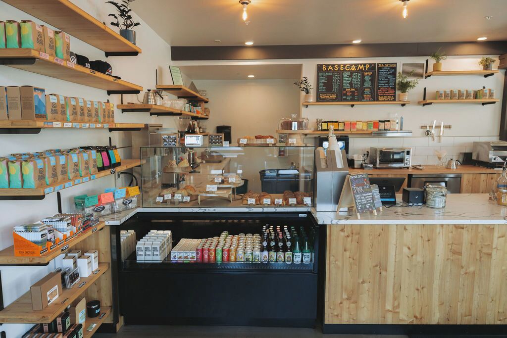 A café interior with shelves stocked with snacks, a refrigerated display case, a coffee machine, and a menu board.