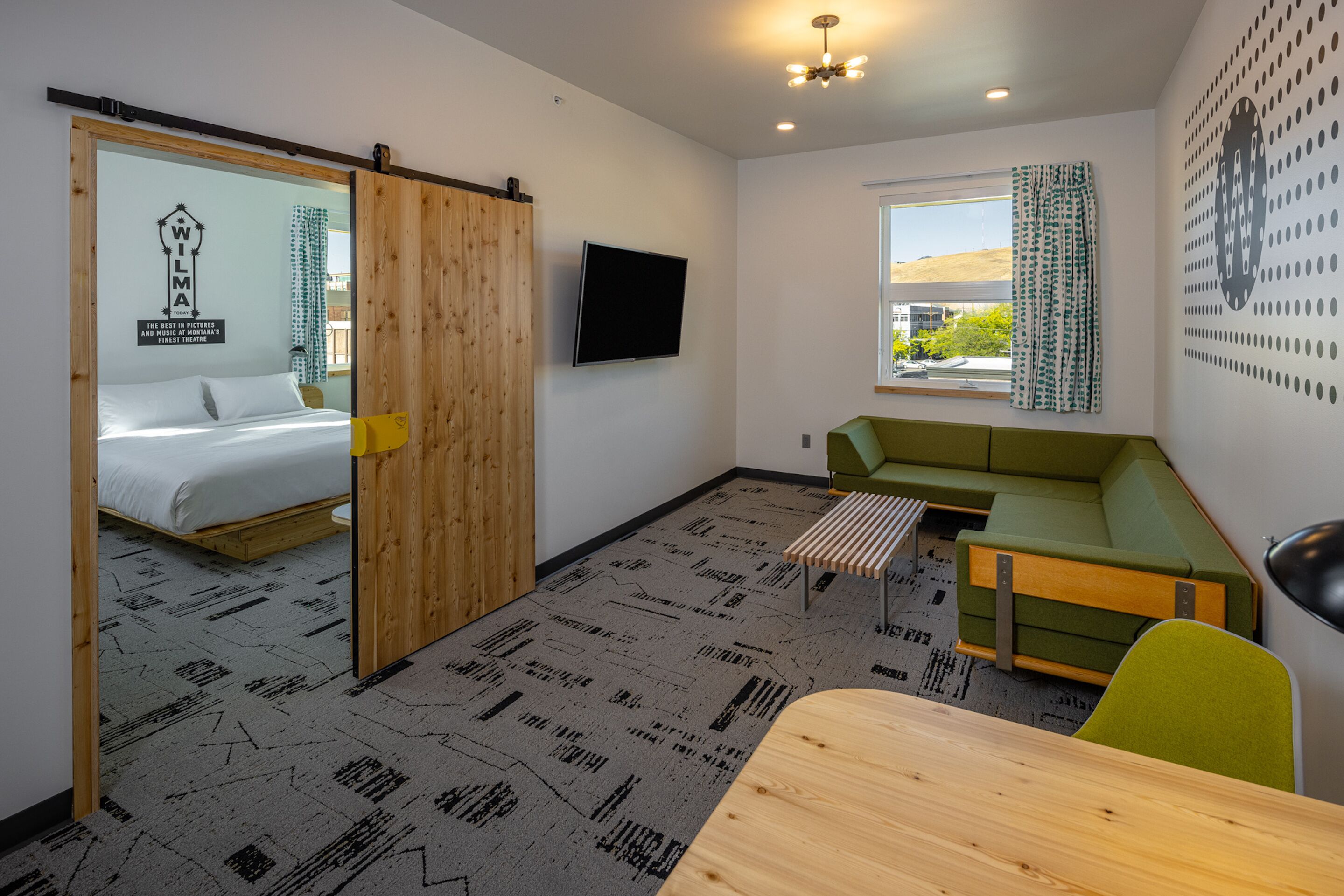 A modern room with a bed, a green sofa, a small table, and a TV.