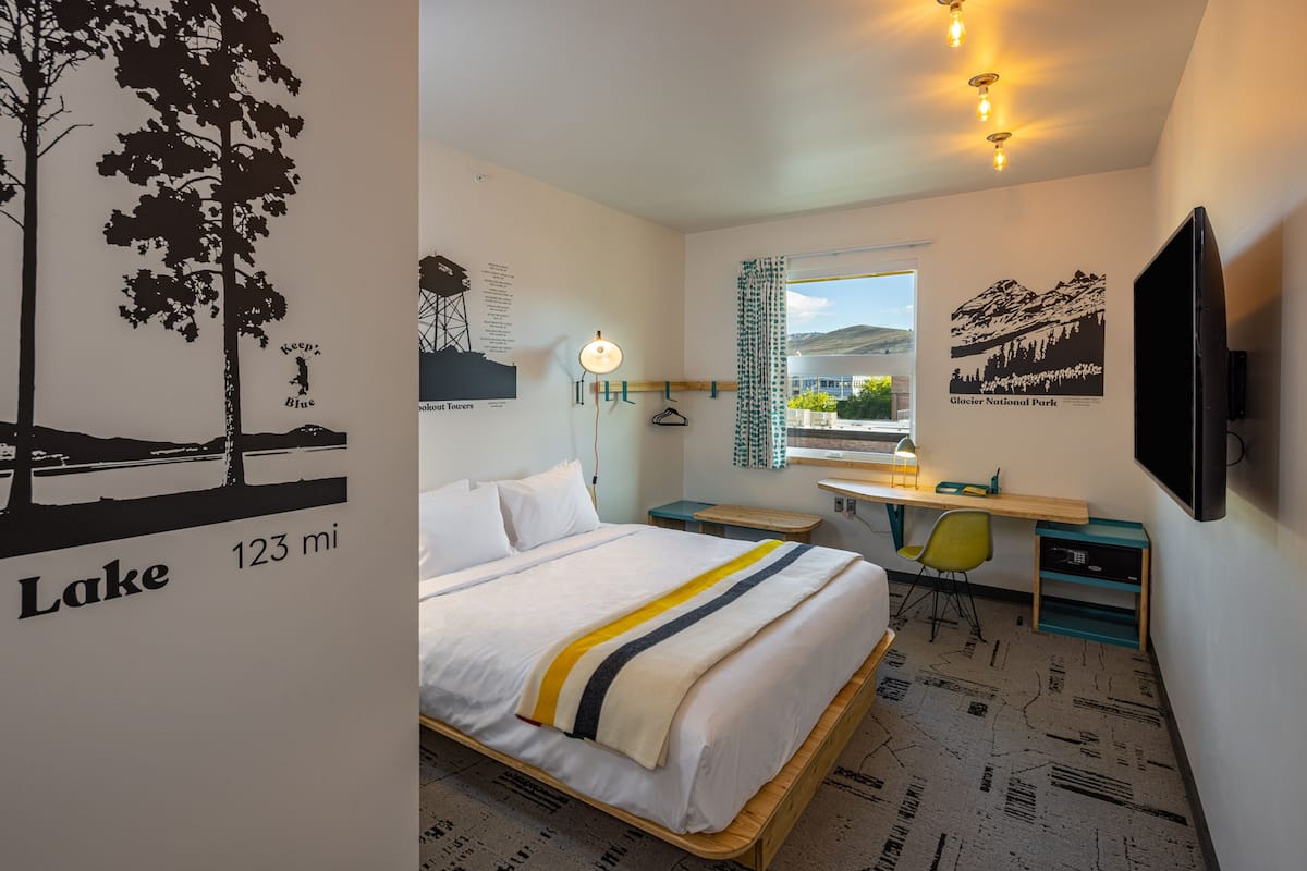 A hotel room with a bed, desk, chair, and a TV.