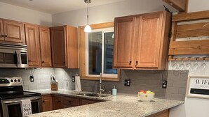 Una cocina con armarios de madera, encimera de granito, horno empotrado, microondas, fregadero y una zona con taburetes de bar.