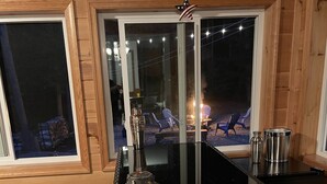 Interior acogedor de una cabaña con una zona de bar de mimbre, dos taburetes acolchados, un ventanal con vistas a una terraza y un cartel de Route 66 en la parte superior.