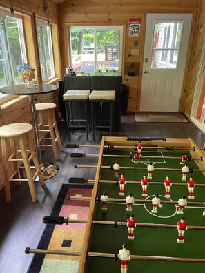 Et hyggeligt rum med et bordtennisbord, træbarmstole og et vindue med udsigt til en have.