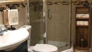 Une salle de bain avec une douche à parois de verre, des toilettes blanches et un meuble-lavabo avec un miroir.
