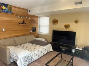 Ein Wohnzimmer mit einer Couch, einem Glastisch, einem Fernseher und dekorativen Wandbildern.