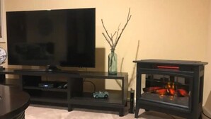 Un salon avec un téléviseur à écran plat posé sur un meuble, une petite table sur laquelle se trouve un vase, et une cheminée avec des lumières rouges.