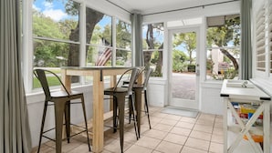 A room with a wooden table and metal chairs, large windows with curtains, and a view of trees and a building outside. - Classic Seagrove Cottage One Block from 30A Beach Access (Santa Rosa Beach)