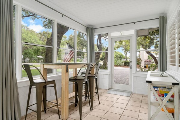 A room with a wooden table and metal chairs, large windows with curtains, and a view of trees and a building outside. - Classic Seagrove Cottage One Block from 30A Beach Access (Santa Rosa Beach)
