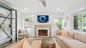 A living room with a fireplace, a sofa, a coffee table, and a TV mounted above the fireplace. - Classic Seagrove Cottage One Block from 30A Beach Access (Santa Rosa Beach)