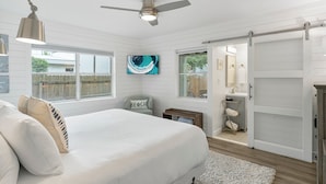 A bedroom with a bed, a ceiling fan, a TV, a sliding door to a bathroom, and a view of the outside. - Classic Seagrove Cottage One Block from 30A Beach Access (Santa Rosa Beach)