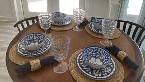 Une table à manger dressée avec des assiettes aux motifs bleus et blancs, de la verrerie transparente et des sets de table en fibres tressées.