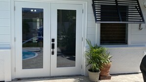 Une maison blanche avec une porte en verre, un auvent noir et deux plantes en pot.