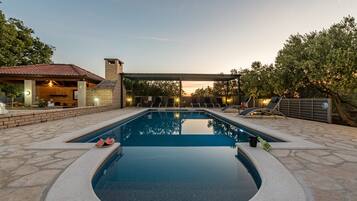 Una piscina con cubierta de piedra, sillas de descanso y un patio techado.