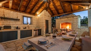 Eine Steinküche mit Kamin, einem Esstisch gedeckt mit Tellern und Gläsern, und einer hängenden Leuchte.