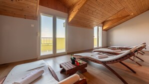 Ein sonnendurchfluteter Raum mit Holzbalken, einem Balkon und Liegestühlen.