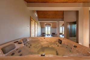 A hot tub in a room with wooden ceiling, a view to a balcony, and a glass shower area.