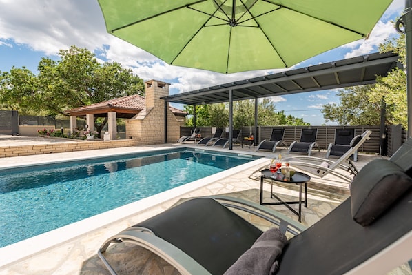 A swimming pool with lounge chairs and a table, surrounded by a covered patio area.