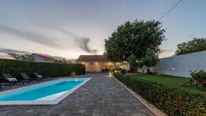 A swimming pool with lounge chairs, a paved walkway, and a house in the background. - Villa Andu Zadarvillas (Škabrnja)
