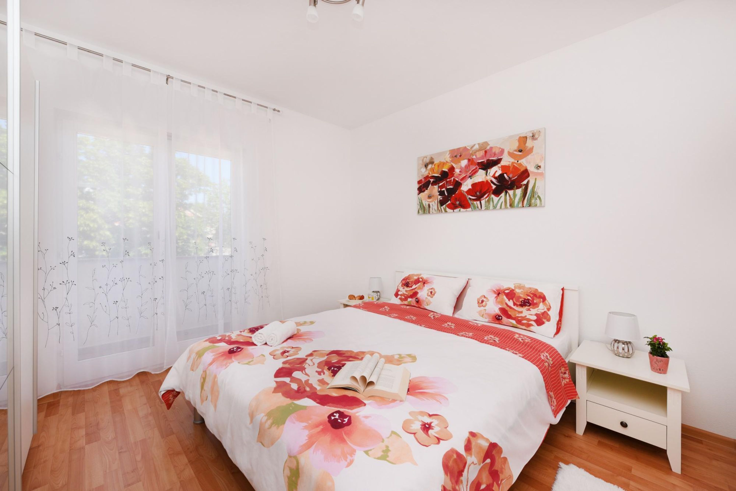 A bedroom with a floral bedspread, a nightstand with a lamp, and a painting on the wall.