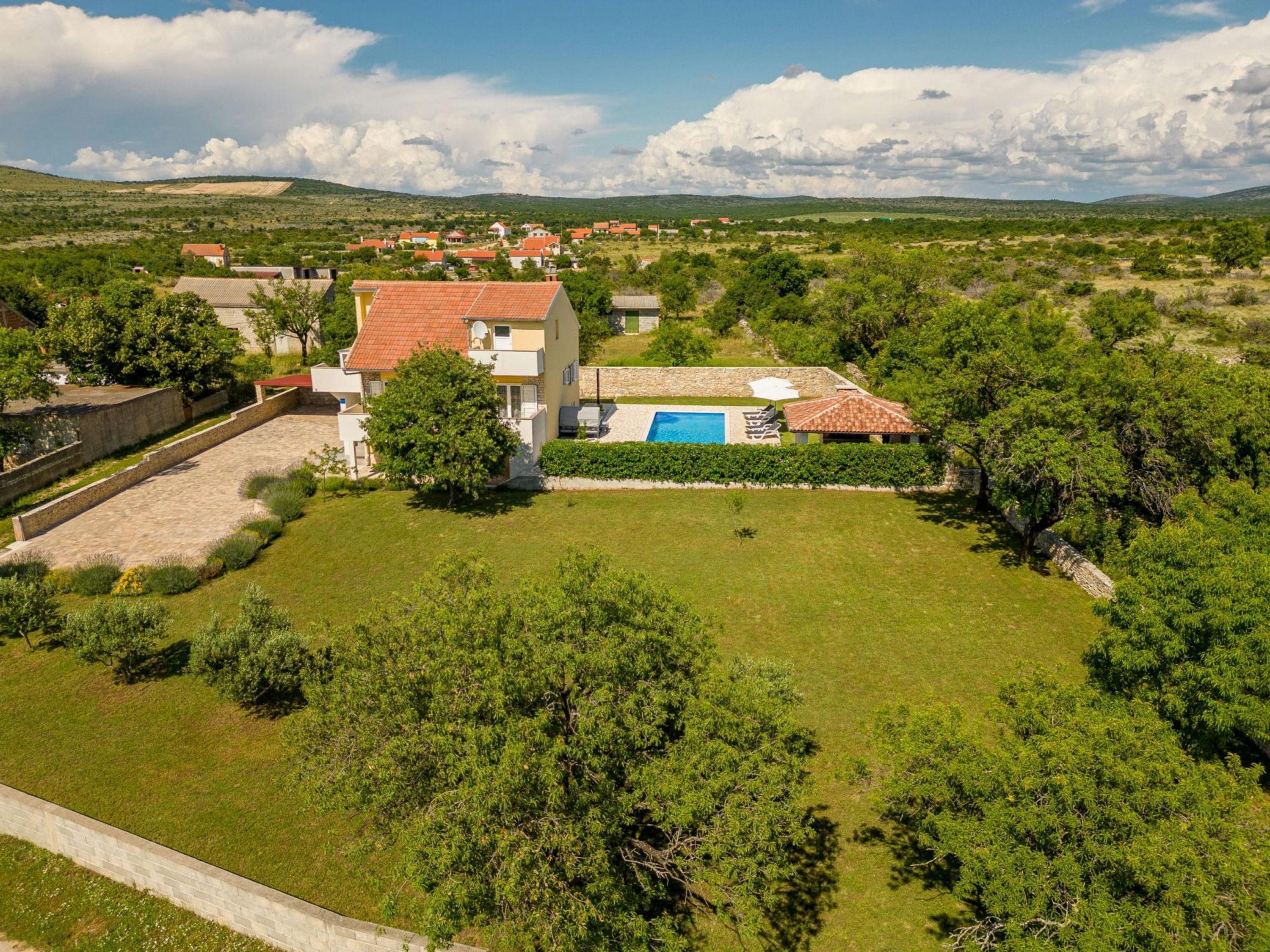 A large house with a swimming pool, surrounded by lush greenery and hills in the background.