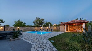 Patio trasero con piscina, terraza de piedra y zona de estar al aire libre cubierta.