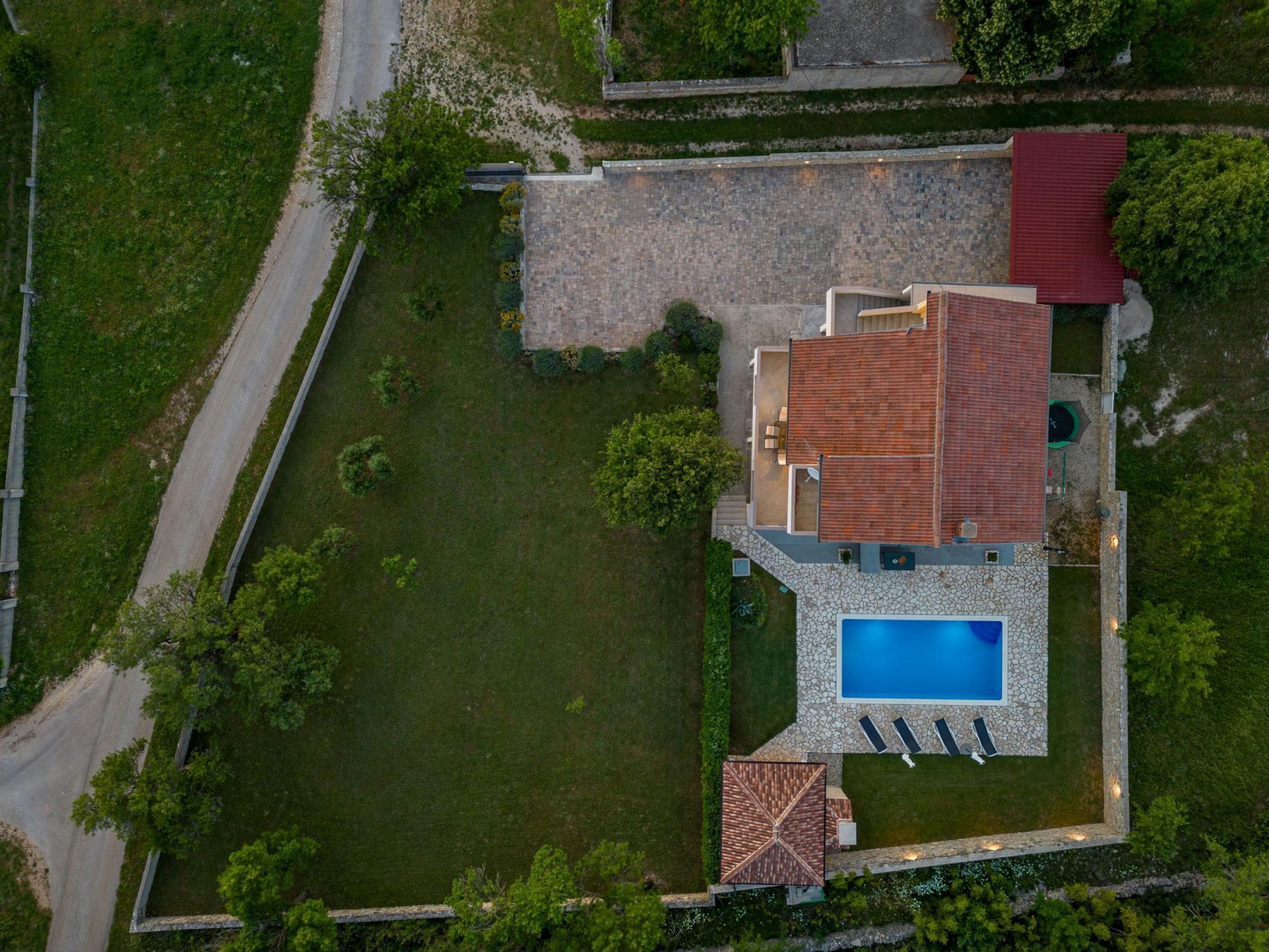 An aerial view of a property with a swimming pool, a patio area, and a stone pathway.