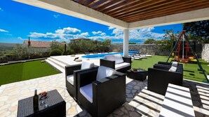 Une terrasse extérieure aménagée avec des meubles en osier, une piscine et une vue sur le paysage.