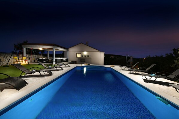 Relax by the rectangular pool surrounded by lounge chairs and a contemporary house with a sauna or hot tub.