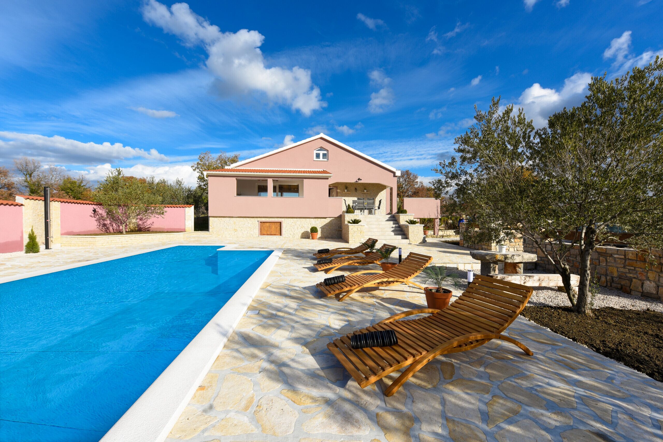 A swimming pool with lounge chairs and a building with a pink facade.