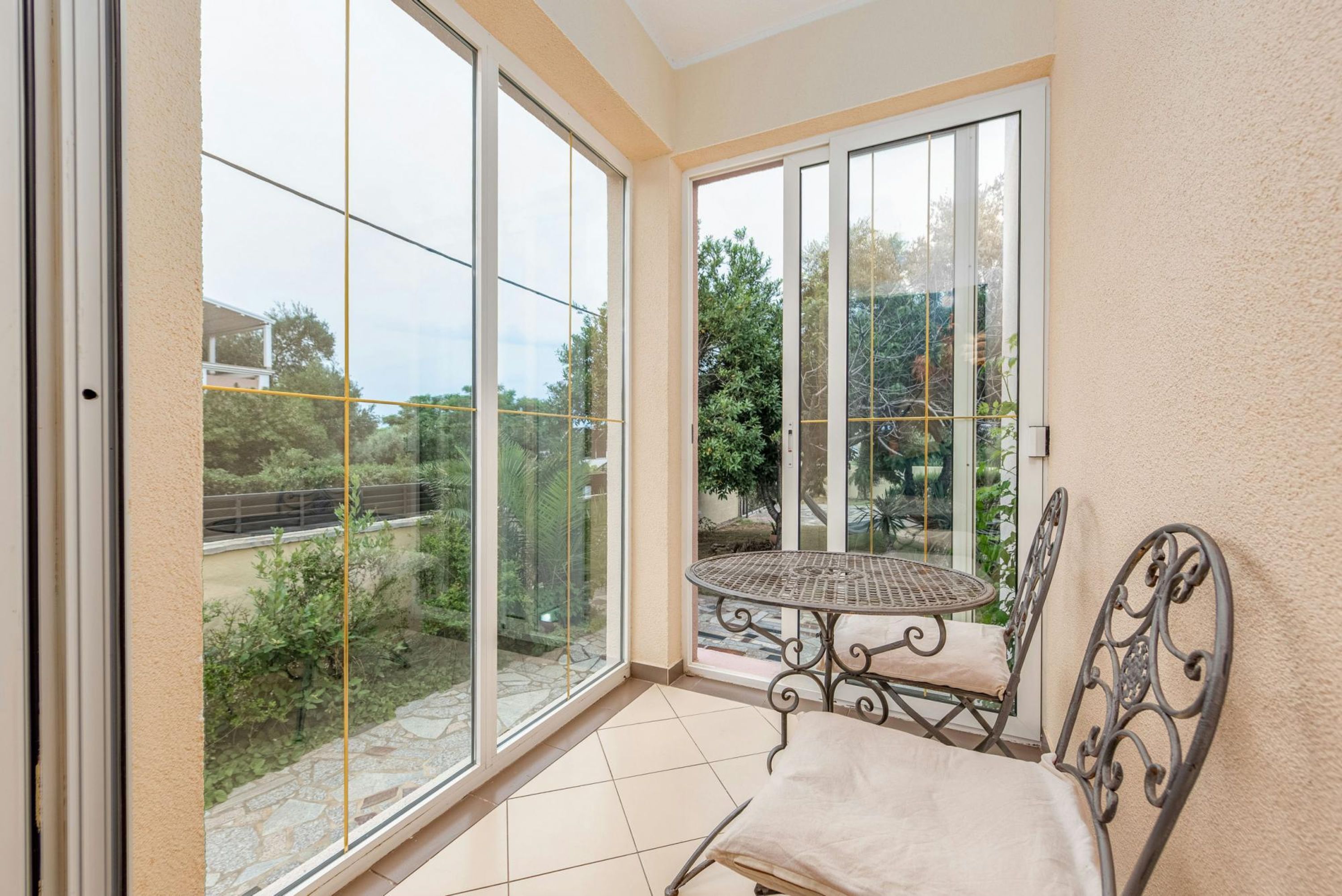 A balcony with a metal table and chair, large sliding glass doors, and a view of greenery and buildings.