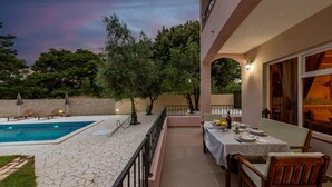 Un espace aménagé au bord de la piscine, avec une table dressée pour les repas, entouré d’un sol en pierre et de mobilier en bois.