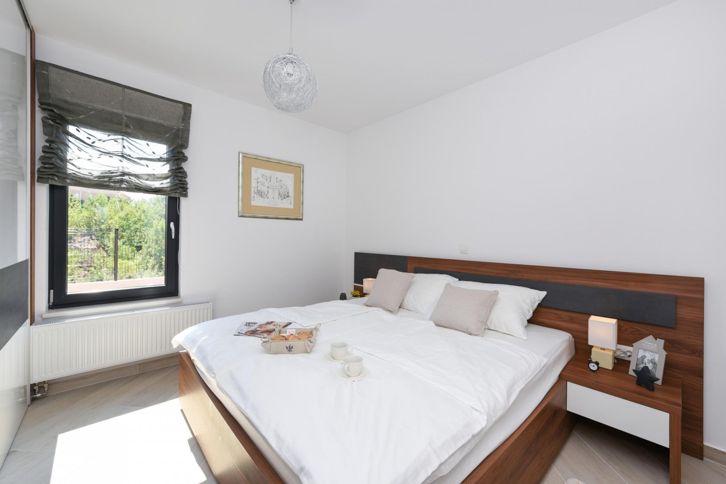 Un dormitorio moderno con una cama grande, una mesita de noche con lámpara y una ventana con vista a zonas verdes.