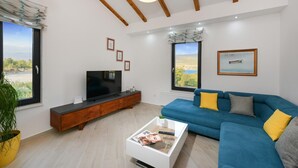 Ein modernes Wohnzimmer mit einem blauen Sofa, einem Couchtisch, einem Fernseher und einem großen Fenster mit Blick ins Freie.