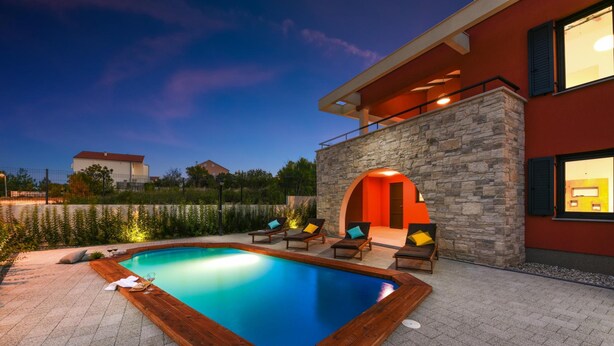 Ein moderner Poolbereich im Freien mit einer Steinwand, Liegestühlen und einer Holzterrasse.