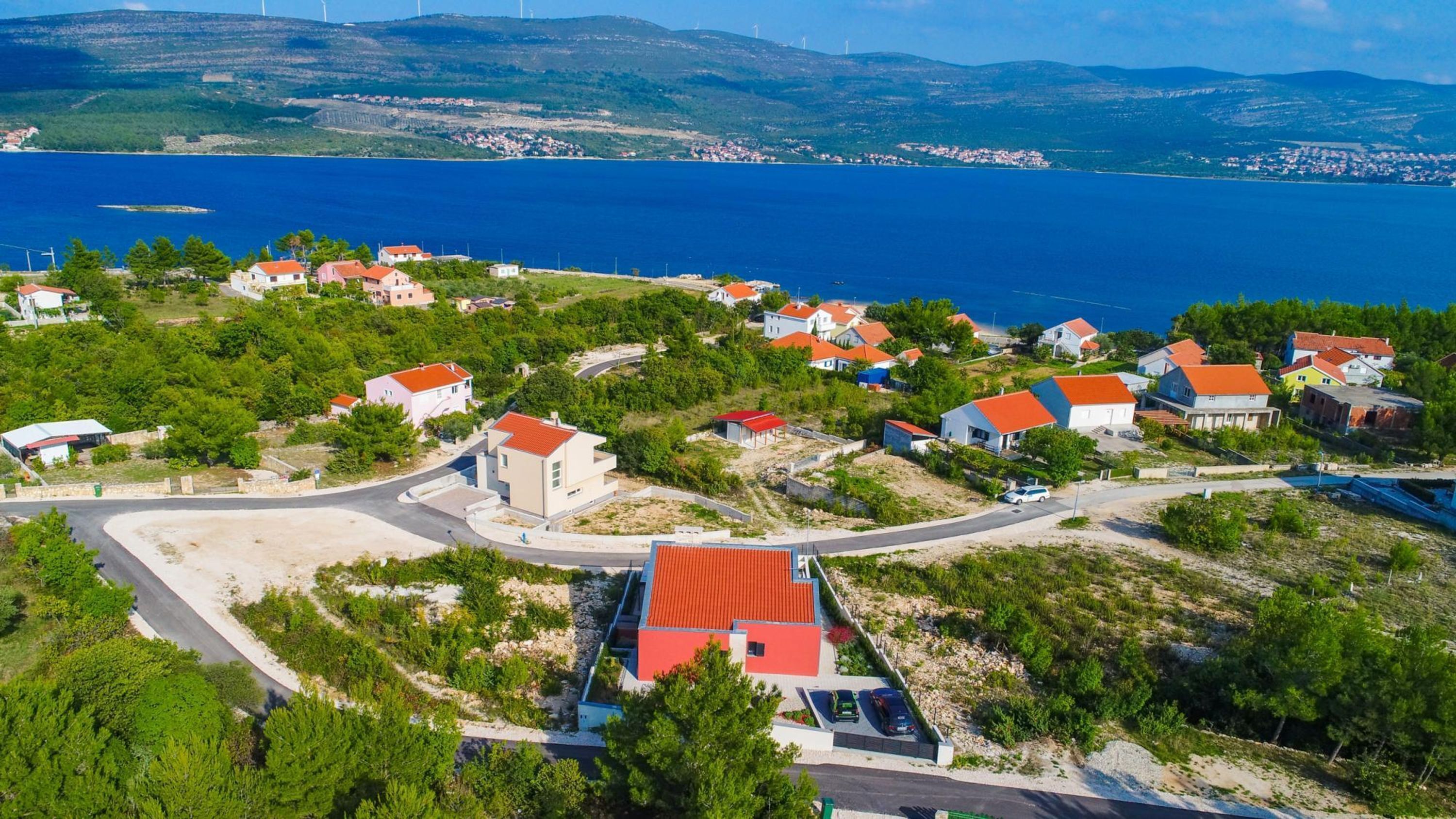 A coastal village with houses, a winding road, and a view of the sea and hills.