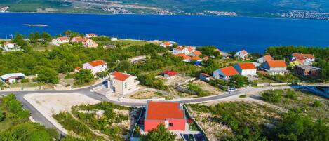 A coastal village with houses, a winding road, and a view of the sea and hills.