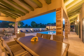 An outdoor dining area with a pool, stone walls, and a view of the surrounding landscape.