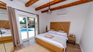 A bedroom with a large bed, a wooden headboard, a nightstand, a mirror, and a view of a swimming pool. - Villa Idassa Zadarvillas (Policnik)