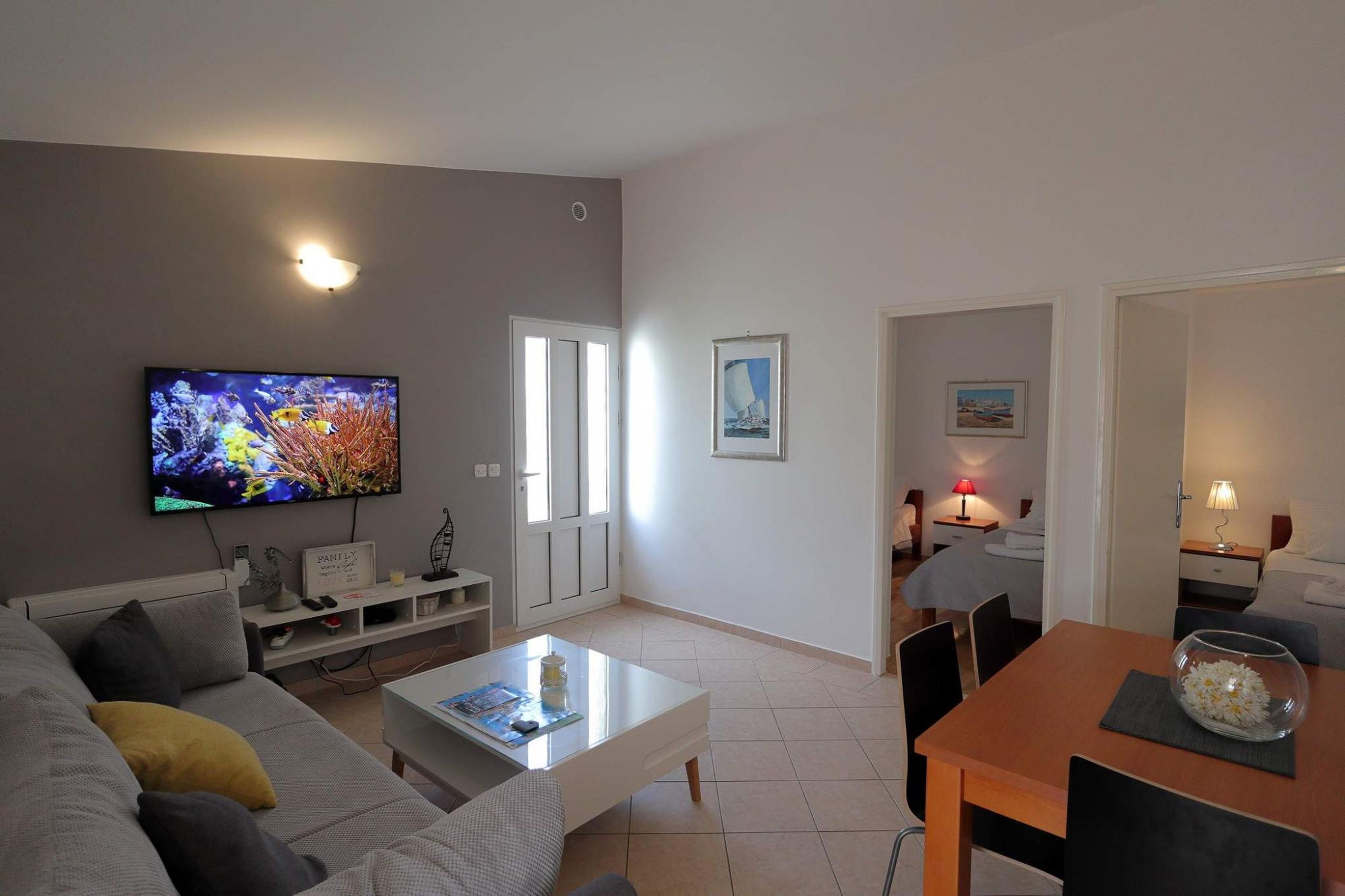 Una sala de estar moderna con un televisor de pantalla plana, un sofá, una mesa de centro y un comedor con una mesa y sillas.