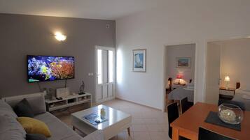 Una sala de estar moderna con un televisor de pantalla plana, un sofá, una mesa de centro y un comedor con una mesa y sillas.