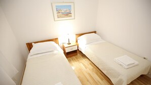 A room with two single beds, wooden flooring, a nightstand with a lamp, and a framed picture on the wall. - Villa Maraschino Zadarvillas (Vir)