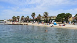 A beach with people sunbathing and swimming, palm trees, and a white van parked on the sand. - Villa Maraschino Zadarvillas (Vir)