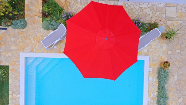A swimming pool with a red umbrella, surrounded by stone tiles and greenery. - Villa Maraschino Zadarvillas (Vir)