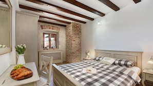 A bedroom with a checkered bedspread, a wooden headboard, a brick wall, and a window with a view. - Villa Laurana Zadarvillas (Pakostane)