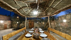 An outdoor dining area with a wooden table set for six, surrounded by stone walls and a thatched roof. - Villa Laurana Zadarvillas (Pakostane)