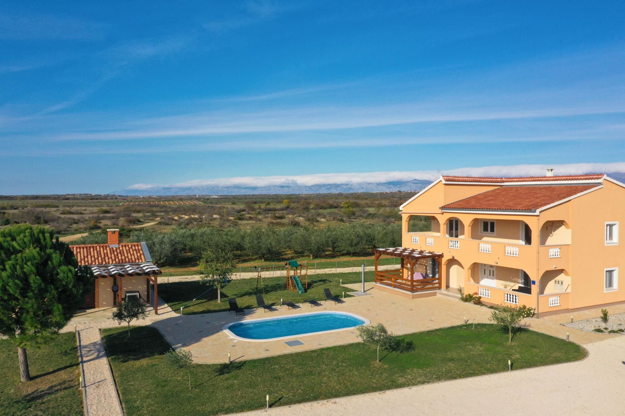 Un edificio grande con piscina, area salotto all'aperto e vista sulle montagne.