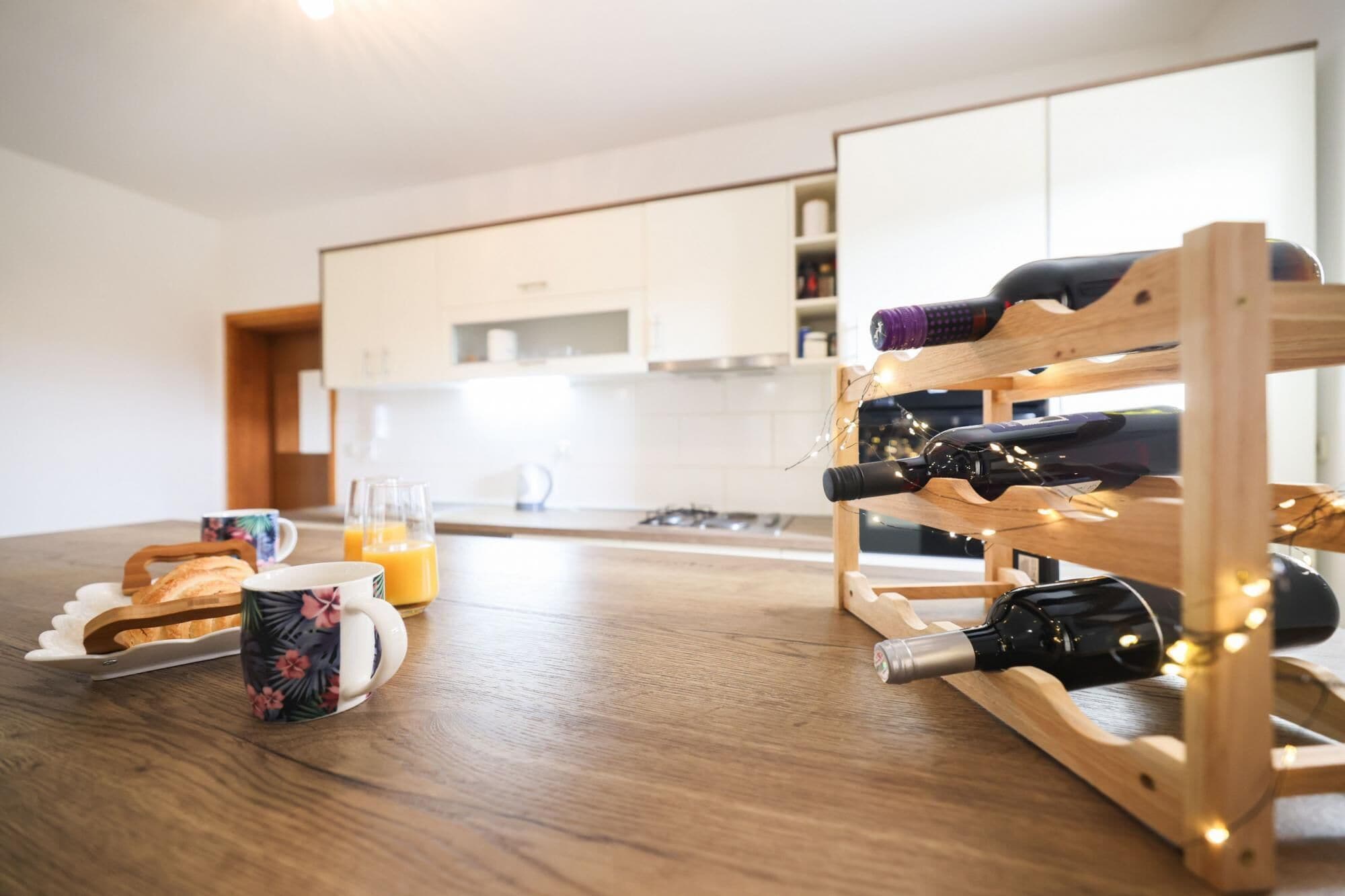 Een moderne keuken met houten meubels, een fruitschaal, een mok met bloemenprint en een wijnrek met flessen.